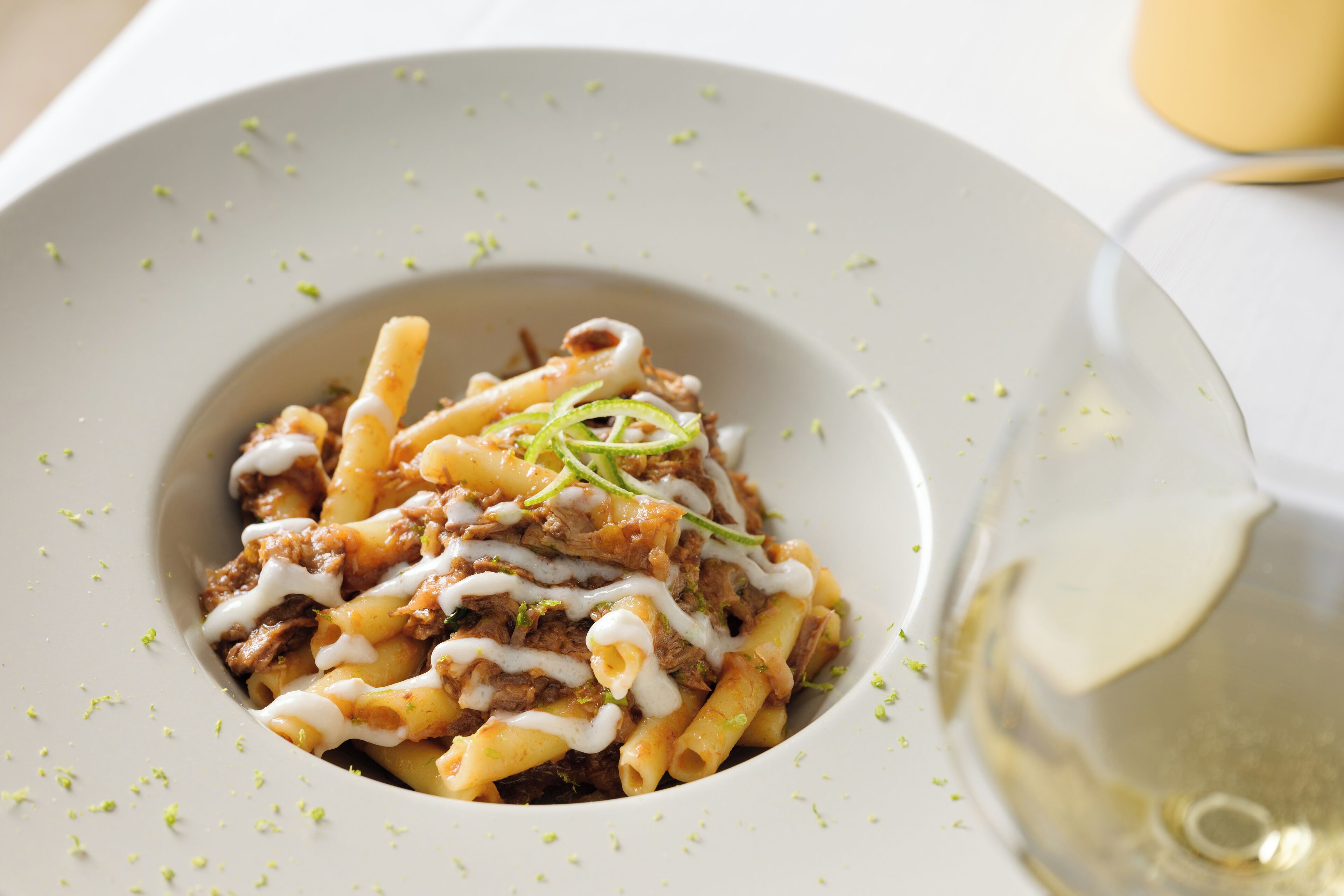 A plate of pasta with meat and a glass of white wine.