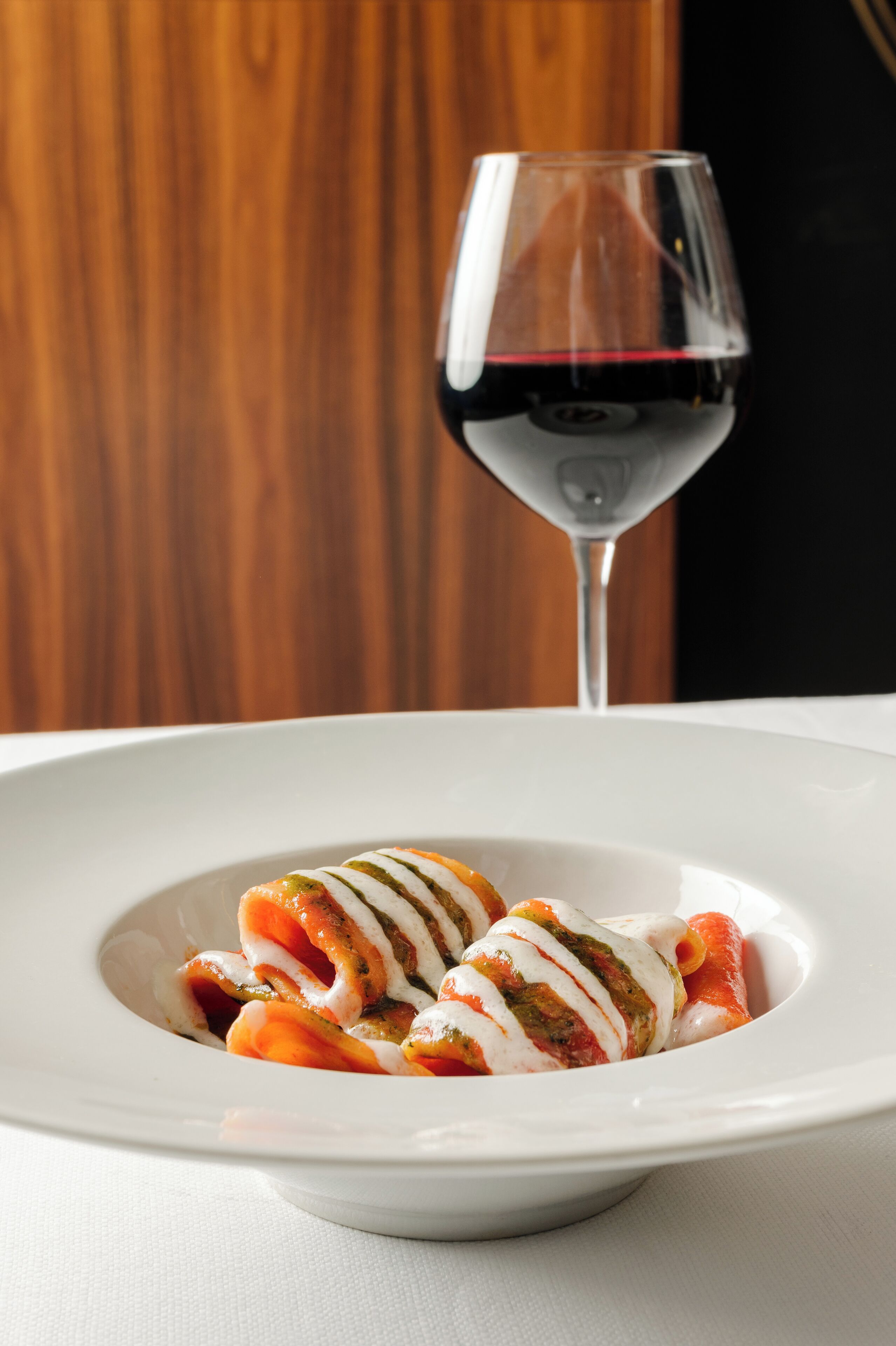 A white plate with a dish of food and a glass of red wine.
