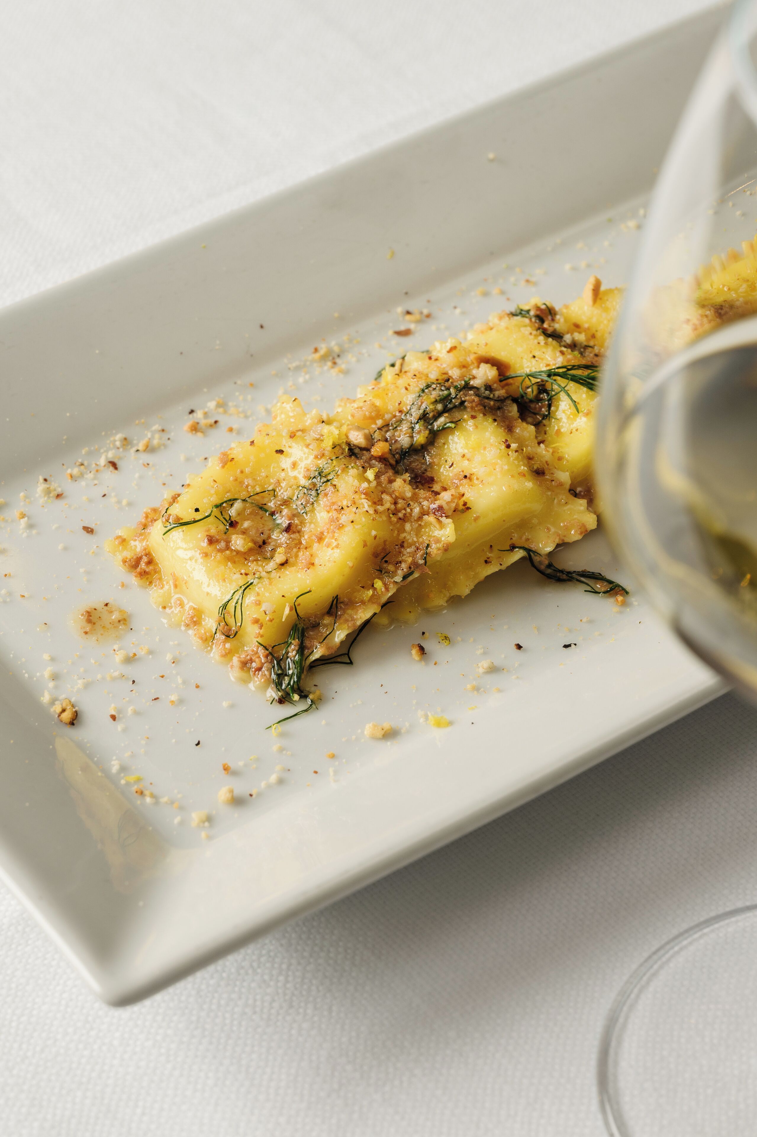 Um prato retangular branco com um pedaço de comida decorado com ervas e migalhas.