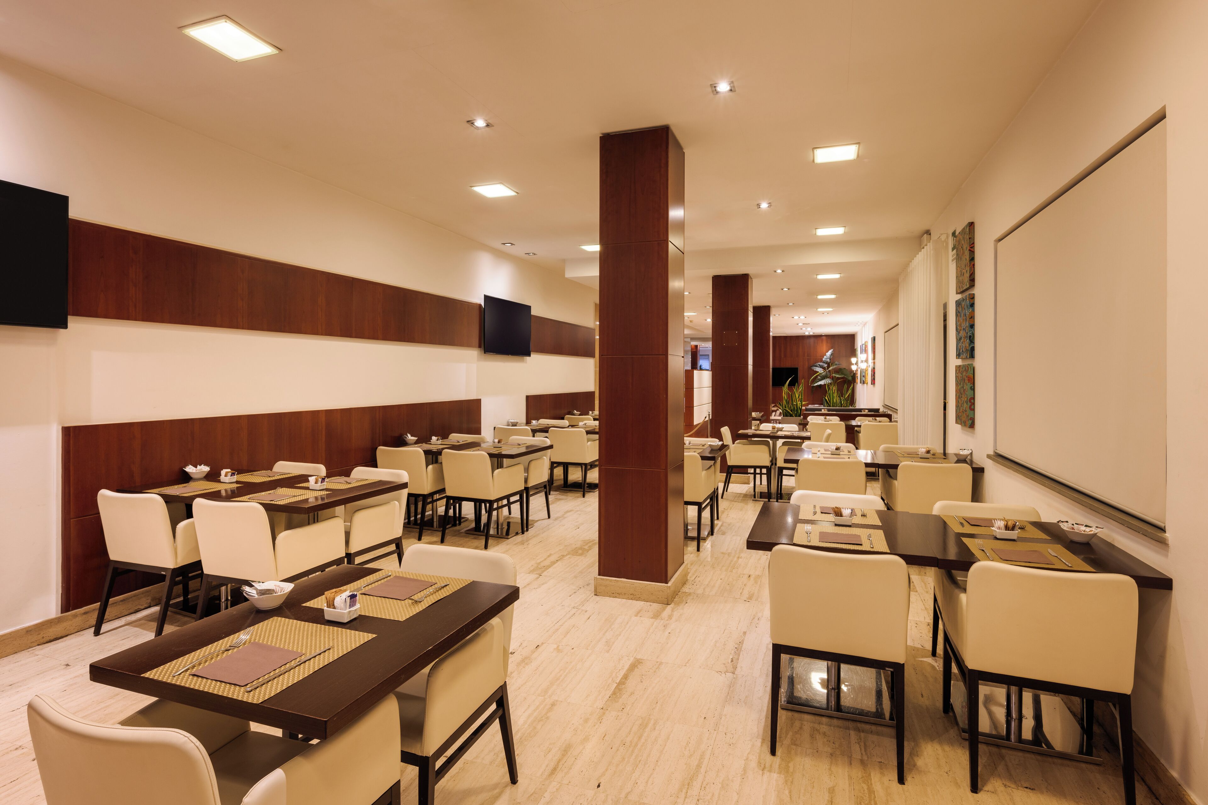 A hotel conference room with multiple tables, chairs, and a large screen on the wall.