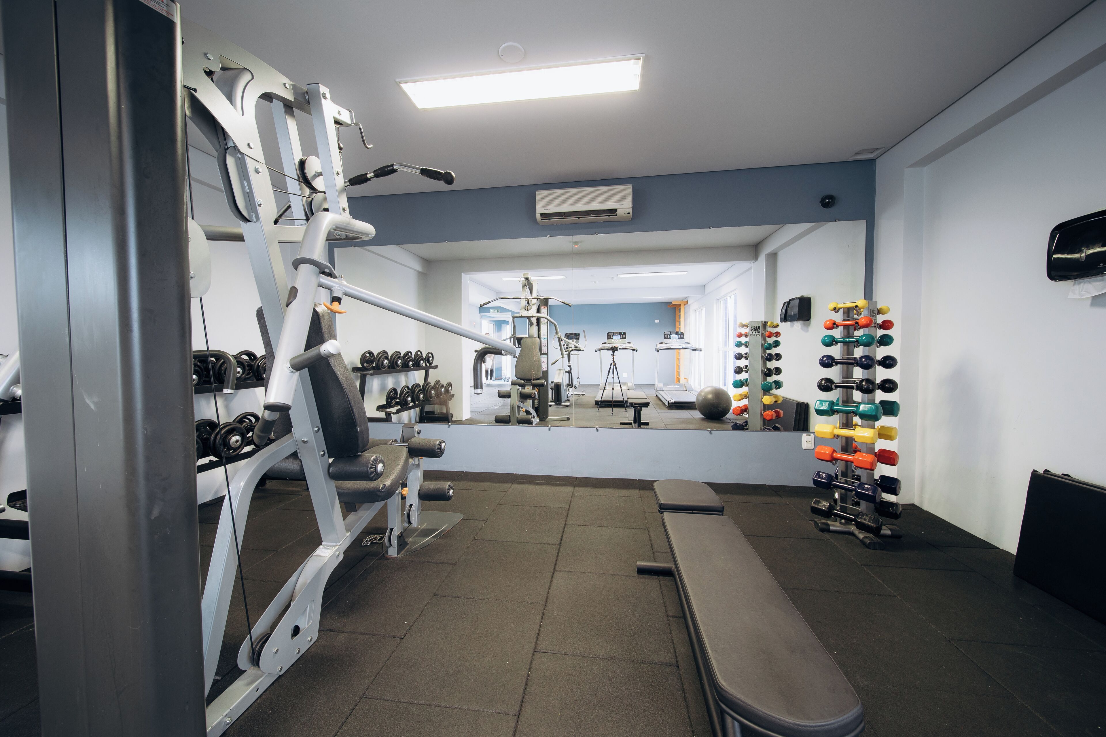 Uma academia com equipamentos de musculação, um banco e um espelho.