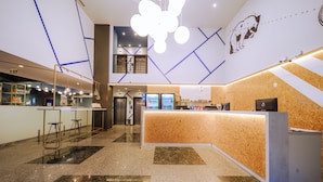 A modern hotel lobby with a reception desk, seating area, and a staircase leading to an upper level. - Hotel Euro Suite Curitiba Batel By Nacional Inn (Curitiba)