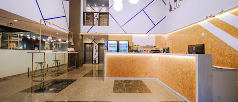 A modern hotel lobby with a reception desk, seating area, and a staircase leading to an upper level.