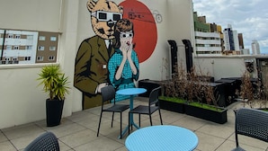A rooftop terrace with a mural, outdoor seating, and a cityscape in the background. - Hotel Euro Suite Curitiba Batel By Nacional Inn (Curitiba)