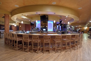 A bar area with a circular bar, wooden chairs, and a wooden floor.