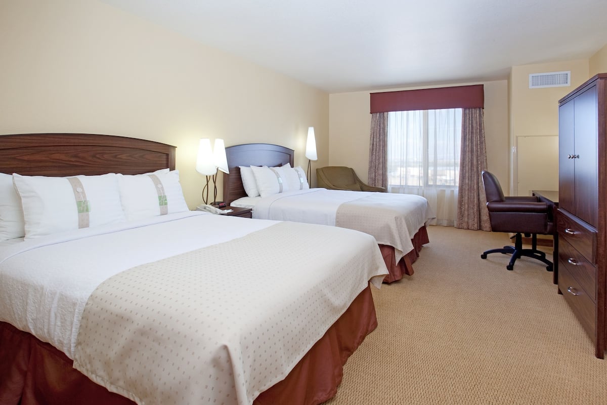A hotel room with two beds, a desk, a chair, and a wardrobe.