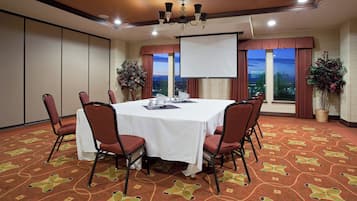 Een congreszaal met een witte tafel, rode stoelen, een scherm voor een projector en uitzicht op de stad in de schemering.