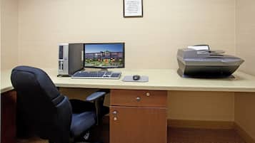 A hotel office with a desktop computer, a printer, a chair, and a framed sign on the wall.