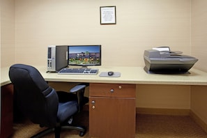 Ein Hotelbüro mit einem Schreibtischcomputer, einem Drucker, einem Stuhl und einem gerahmten Schild an der Wand.