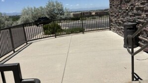 A concrete patio with a stone wall, metal railing, and a clear view of the surrounding landscape.