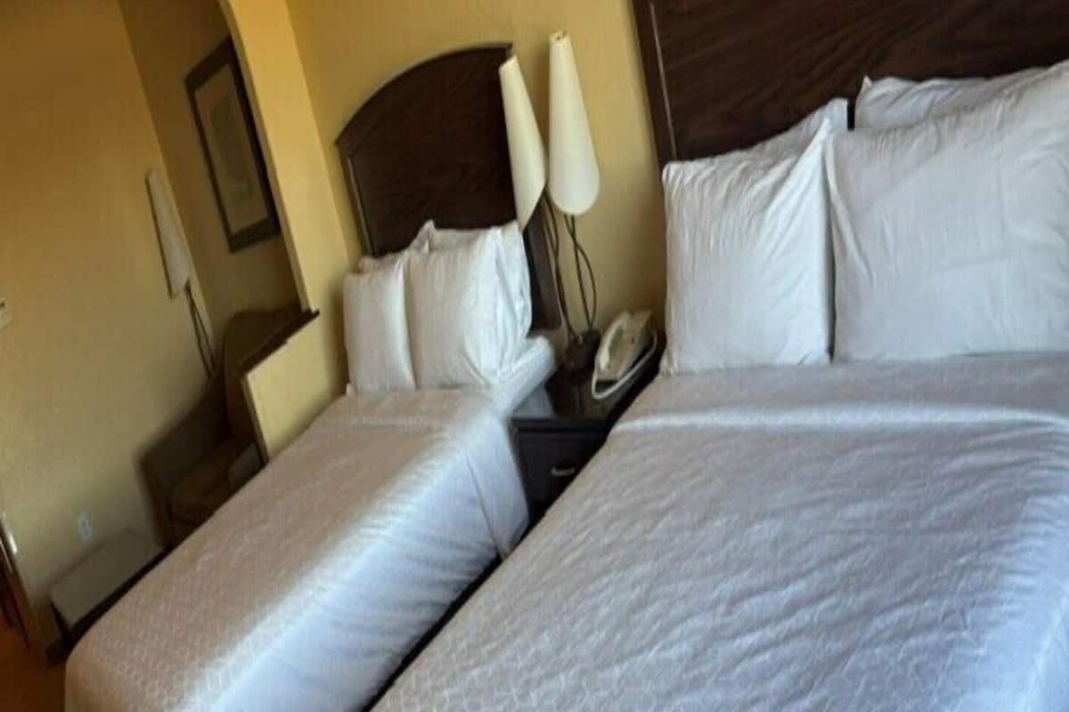 A hotel room with two single beds, a wooden headboard, bedside lamps, and a nightstand.