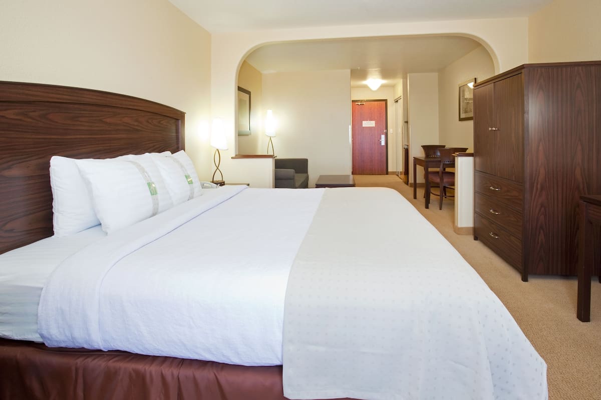 A hotel room with a large bed, a wooden wardrobe, a desk, and a chair.