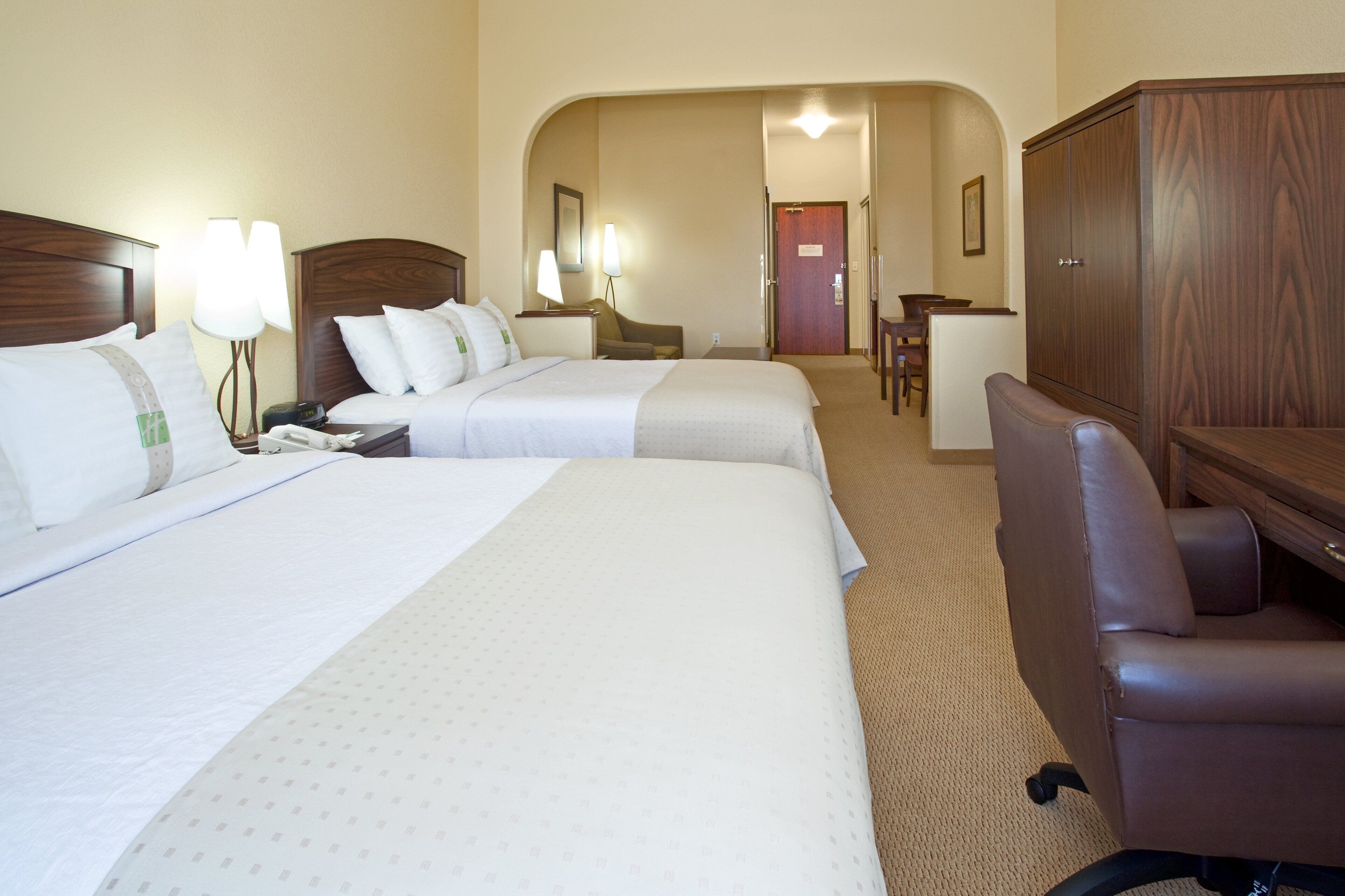 A hotel room with two beds, a desk, a chair, and a wardrobe.