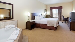 A hotel room with a large bed, a separate desk with a television, a bathroom with a bathtub and towels, and a mirror on the wall.