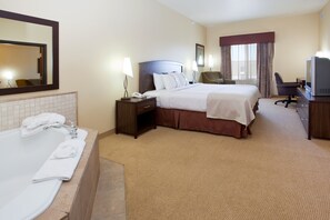 Een hotelkamer met een groot bed, een apart bureau met een televisie, een badkamer met een bad en handdoeken, en een spiegel aan de muur.