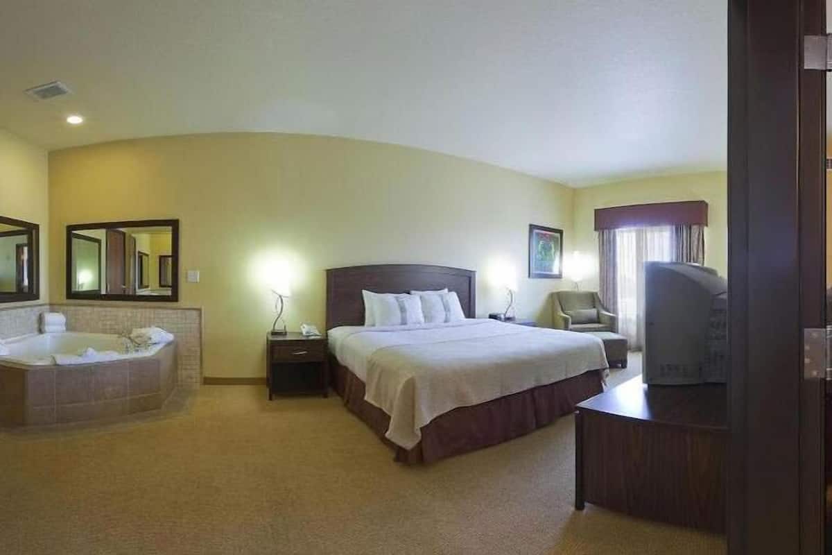A hotel room with a large bed, a sitting area, a TV, and a bathroom with a bathtub and a mirror.