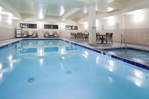 Una amplia piscina interior con agua cristalina, rodeada de sillones y mesas.