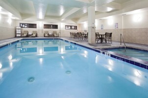 Una amplia piscina interior con agua cristalina, rodeada de sillones y mesas.