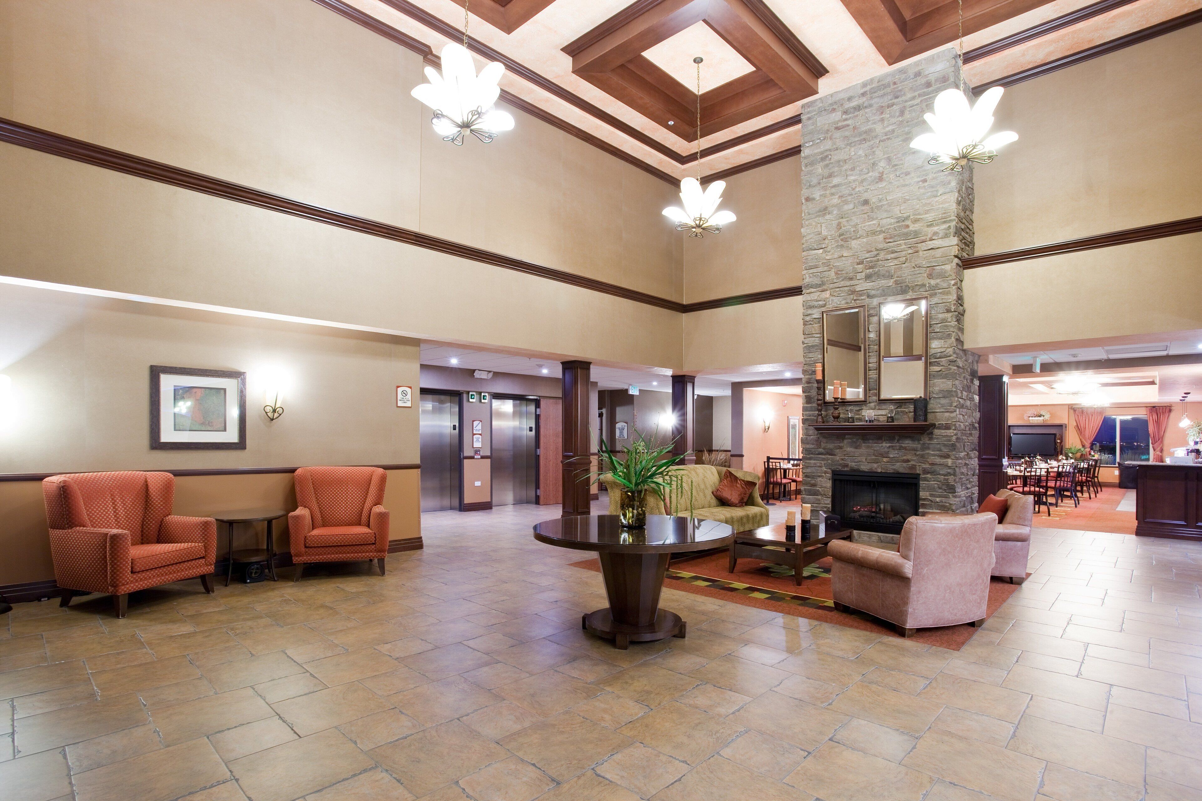 A spacious lobby with a high ceiling, a stone fireplace, and a seating area with armchairs and a coffee table.