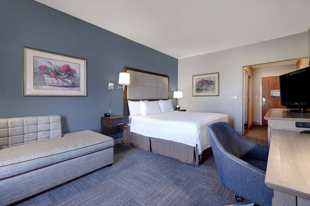 A hotel room with a bed, a sofa, a desk, and a television.