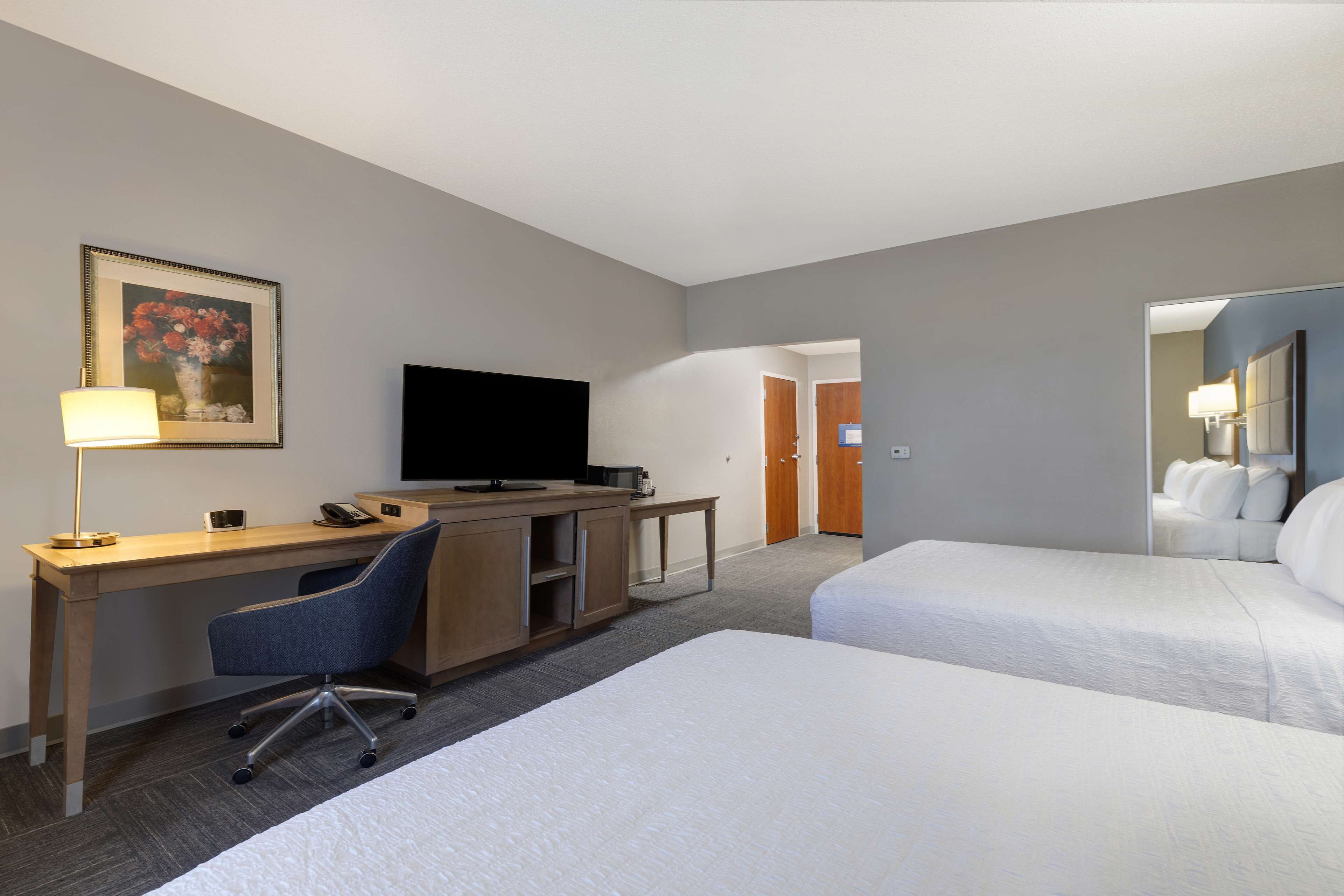 A hotel room with a desk, chair, TV, and two beds.