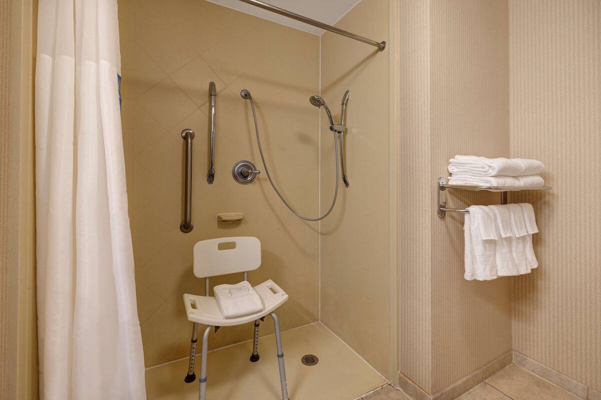 A wheelchair-accessible shower area with a chair, grab bars, and a towel rack.