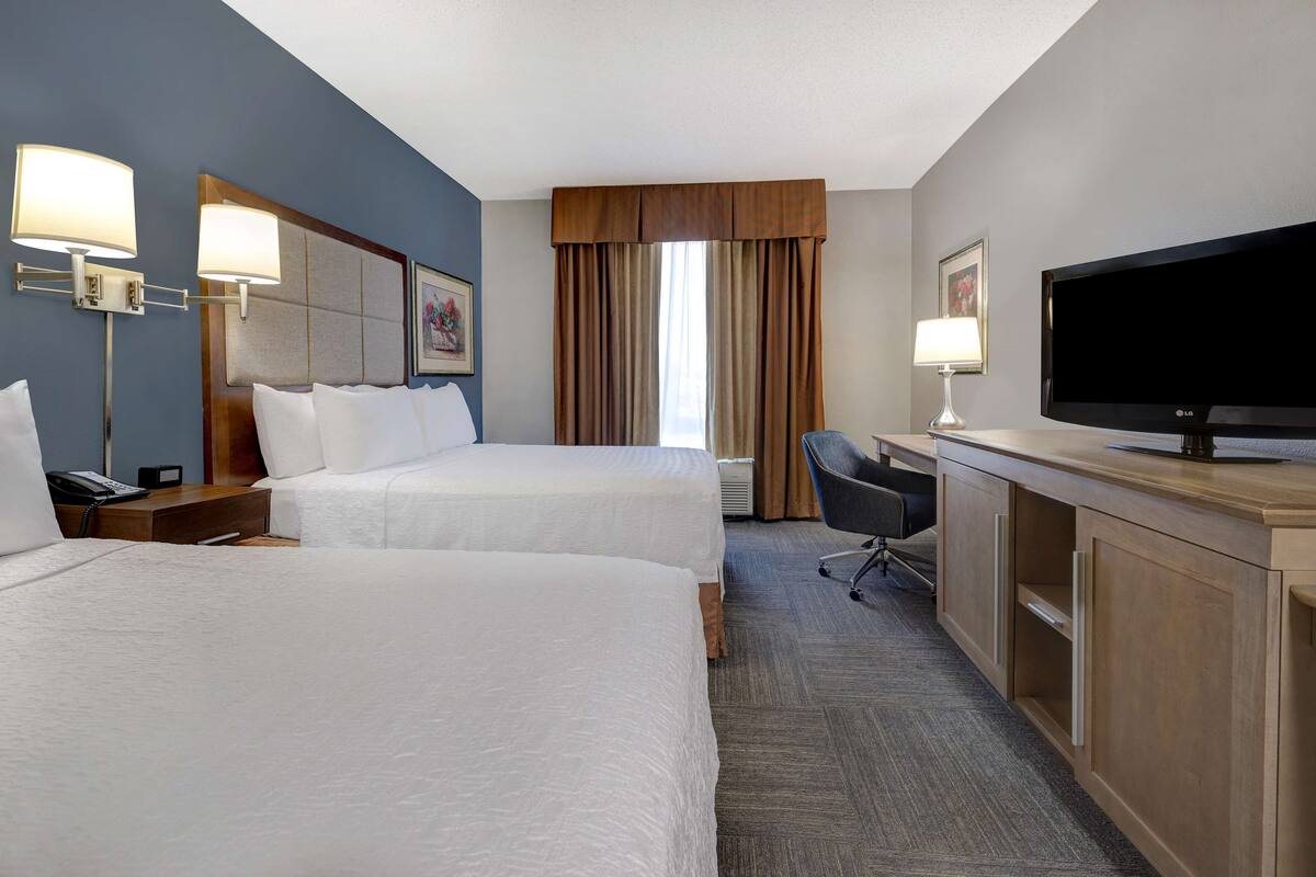 A hotel room with two beds, a desk, a TV, and a chair.