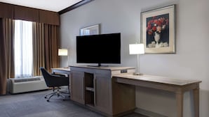 Une chambre d’hôtel équipée d’un bureau, d’un téléviseur à écran plat, d’une chaise, d’une lampe et d’un tableau encadré au mur.
