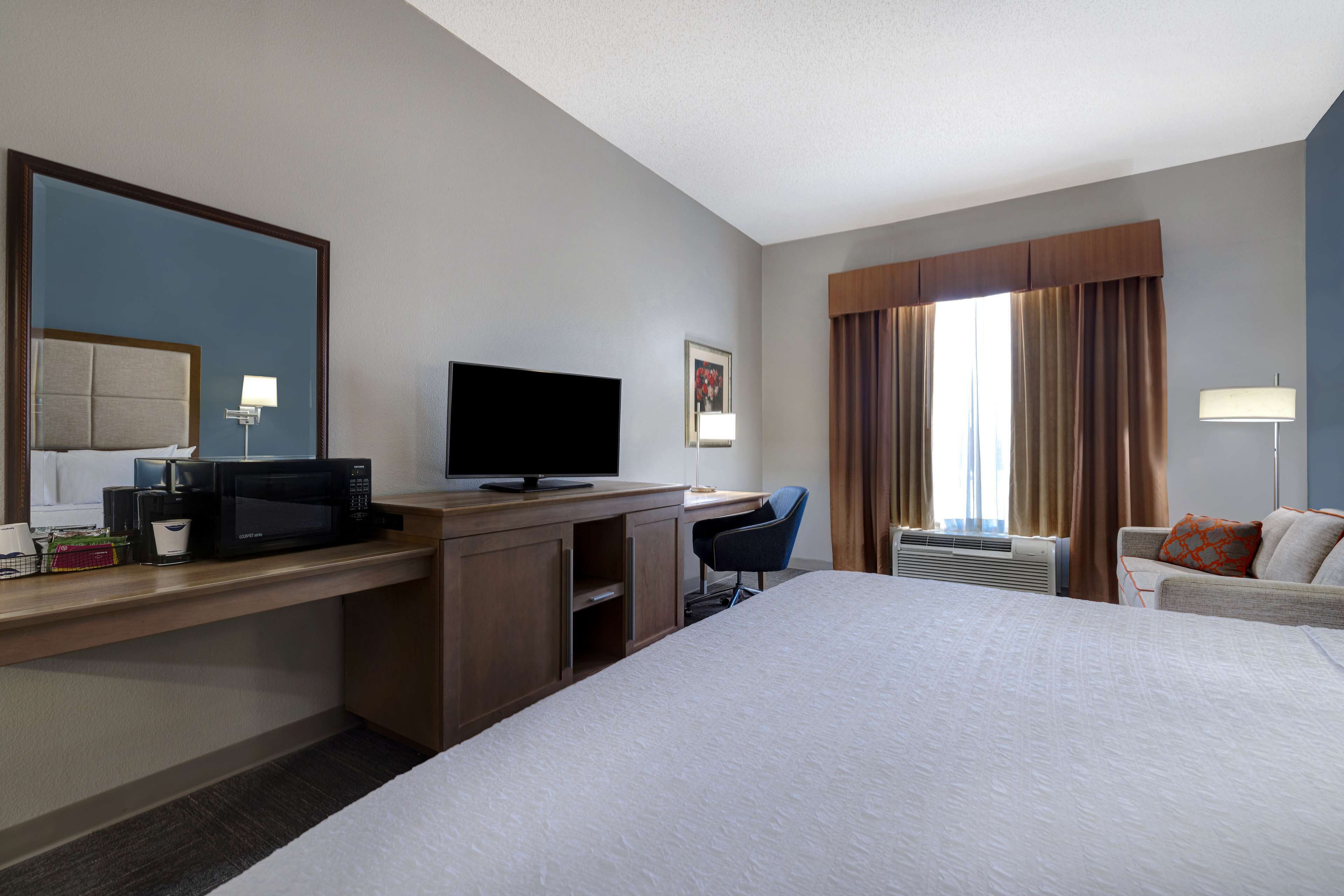 Quarto de hotel com cama, escrivaninha, televisão e uma cadeira.