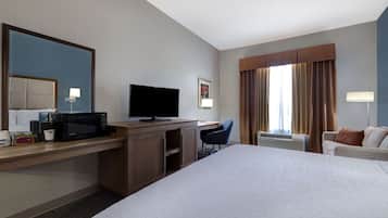 Quarto de hotel com cama, escrivaninha, televisão e uma cadeira.