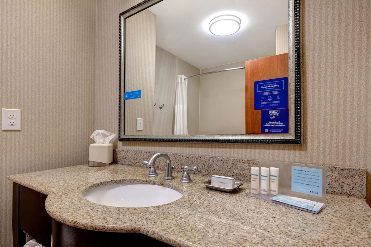 Bany d'hotel amb un lavabo amb taulell de granat, un mirall, un dispensador de tovalloles i productes d'higiene.