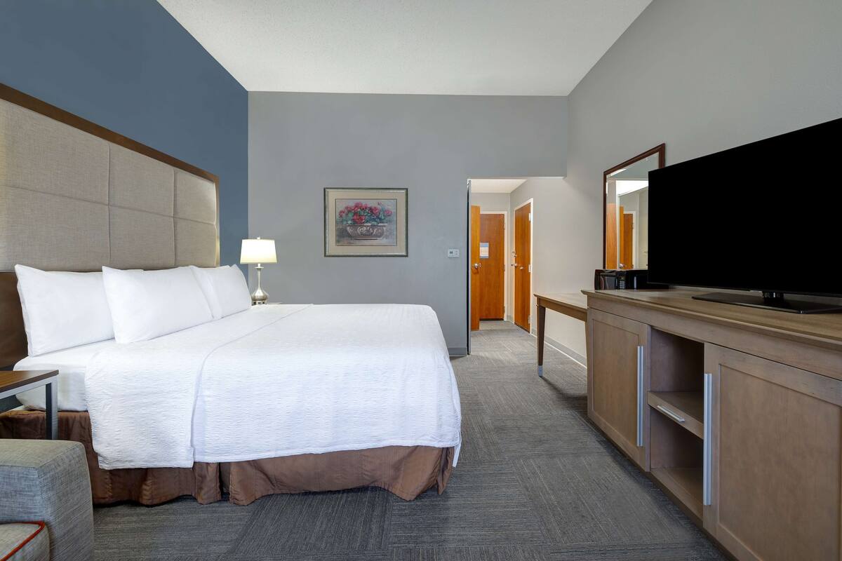 A hotel room with a large bed, a television, a desk with a lamp, and a wooden dresser.