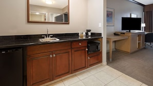 Une chambre d’hôtel compacte dotée d’une kitchenette, d’un grand miroir, d’un téléviseur à écran plat et d’un petit bureau.
