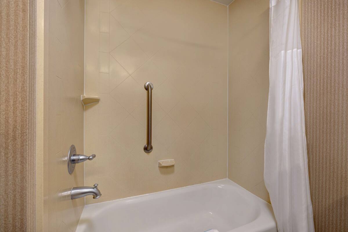 A bathroom with a bathtub, a shower with a grab bar, and a towel rack.