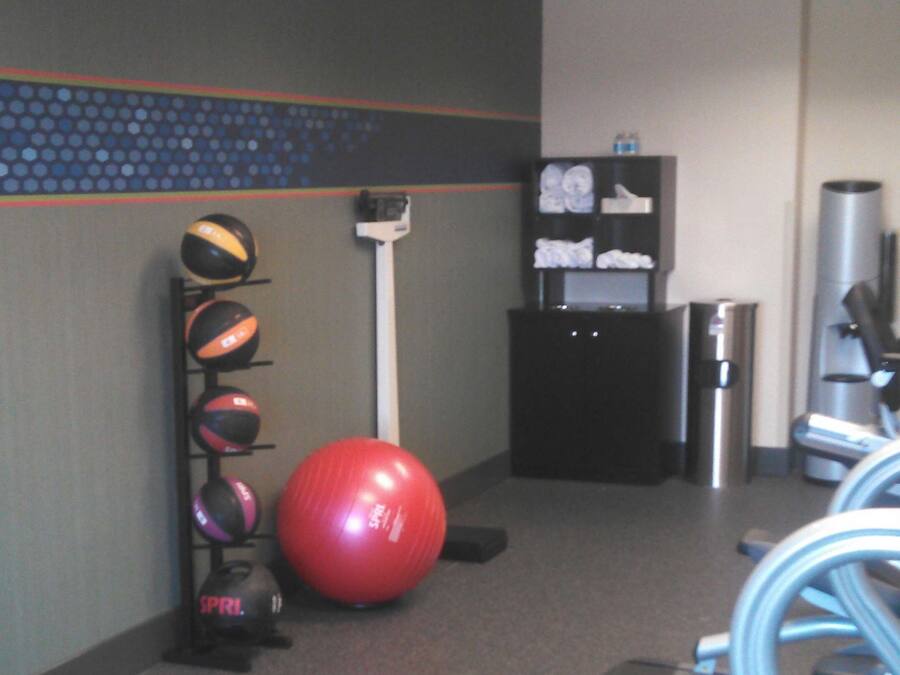 Un gimnasio con equipo de ejercicio, incluyendo una pelota roja, una cinta de correr y un soporte en la pared con diversas pelotas.