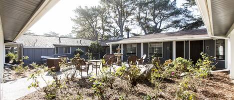 A covered outdoor patio with a seating area, a small garden, and a building with a sloped roof.