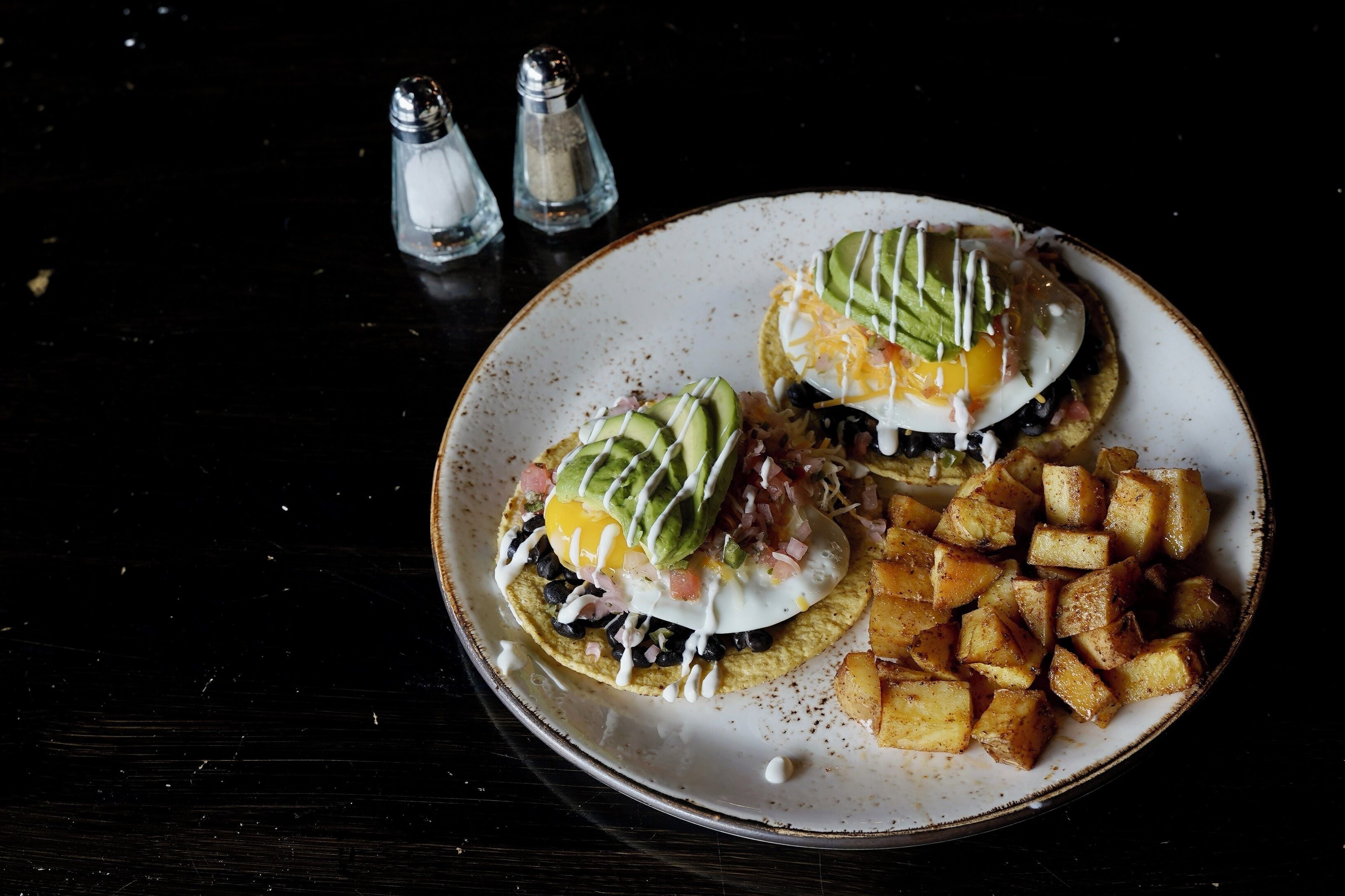 A plate with two eggs benedict, avocado, and diced potatoes.