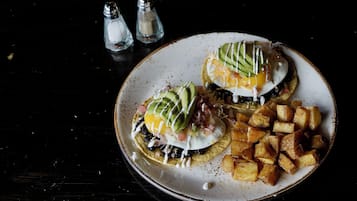 A plate with two eggs benedict, avocado, and diced potatoes.