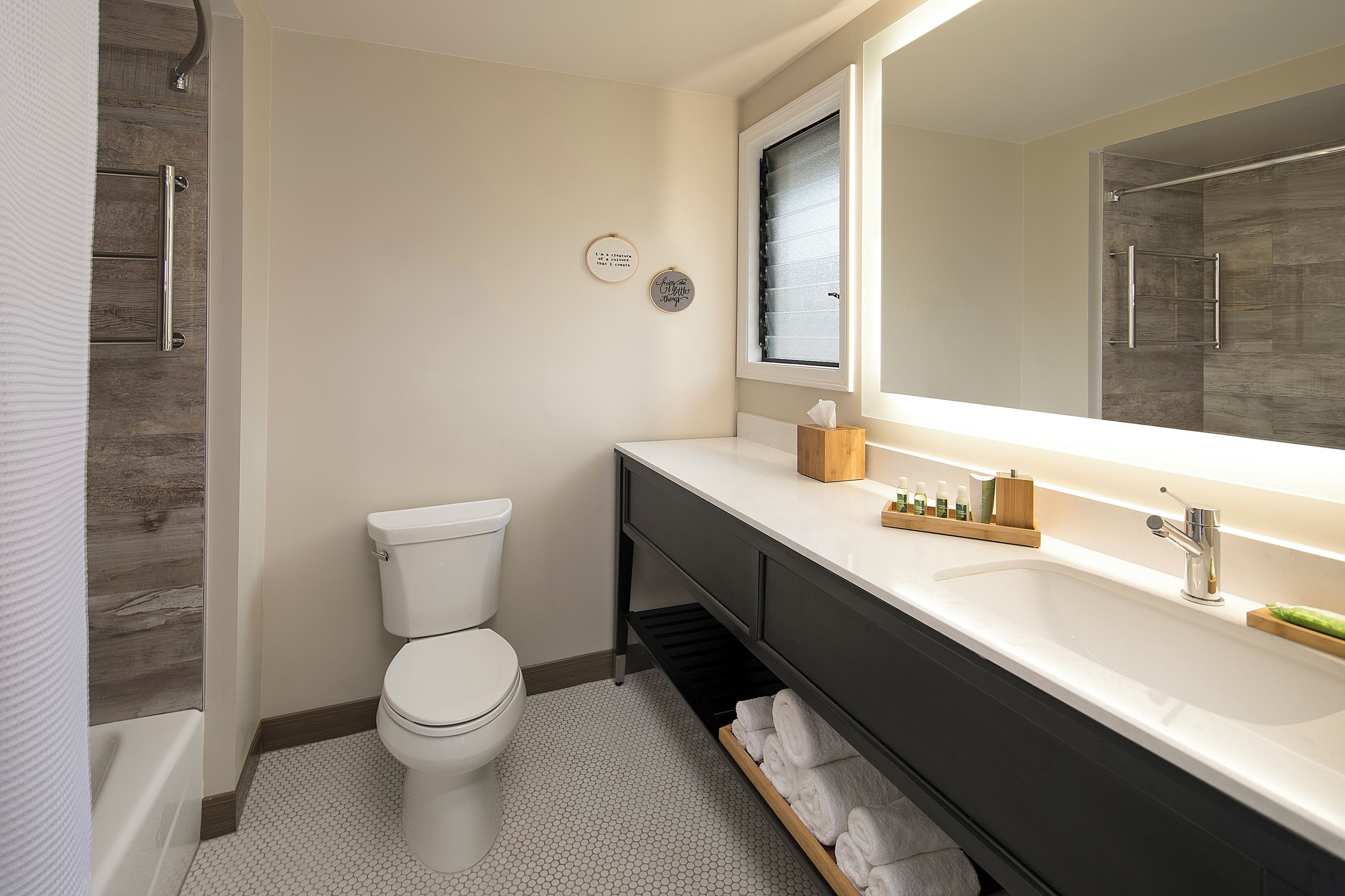 Une salle de bain moderne avec des toilettes blanches, un grand miroir, un meuble-lavabo foncé et un espace douche.