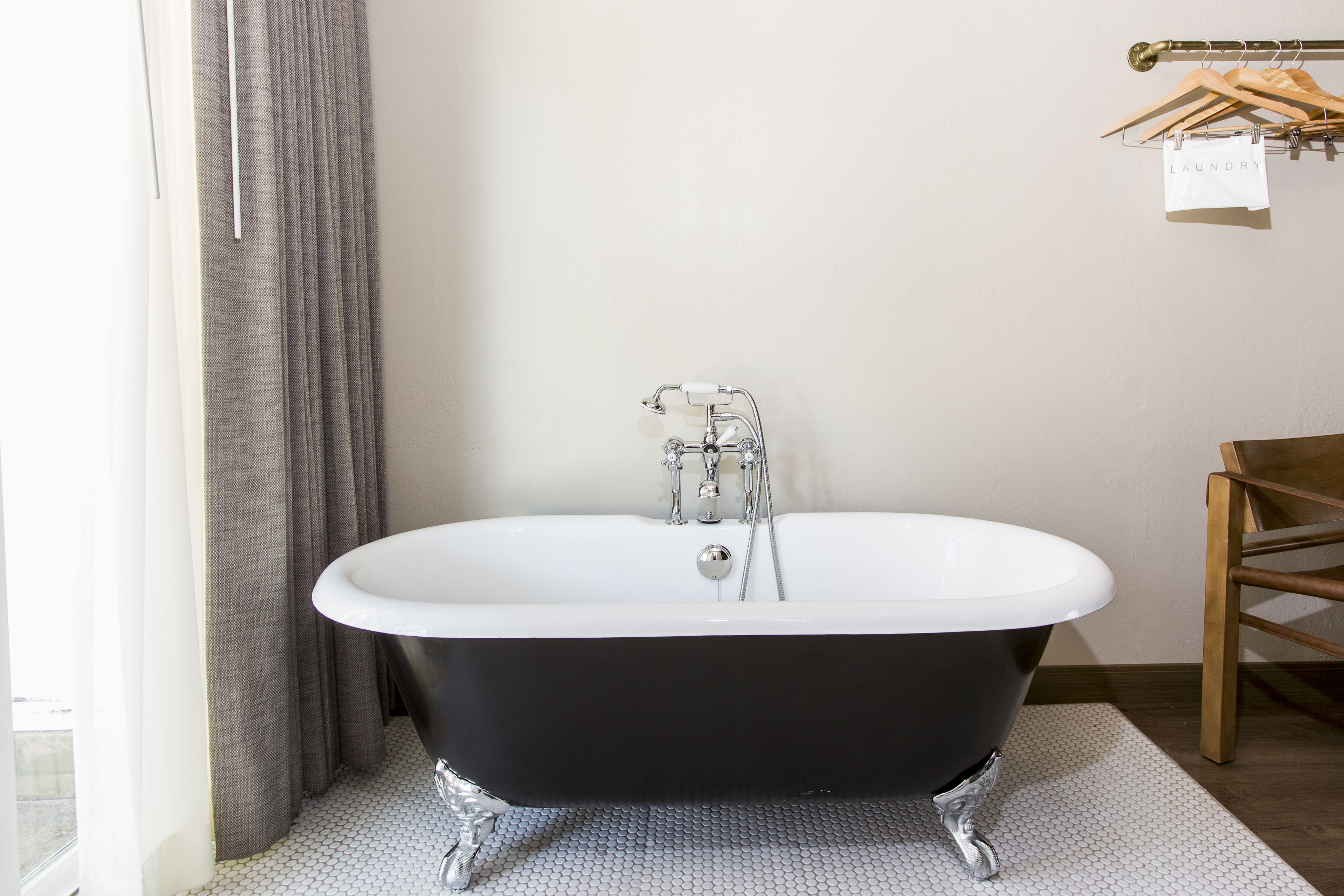 A modern bathroom with a freestanding bathtub, a wooden chair, and a towel rack with a 'laundry' sign.