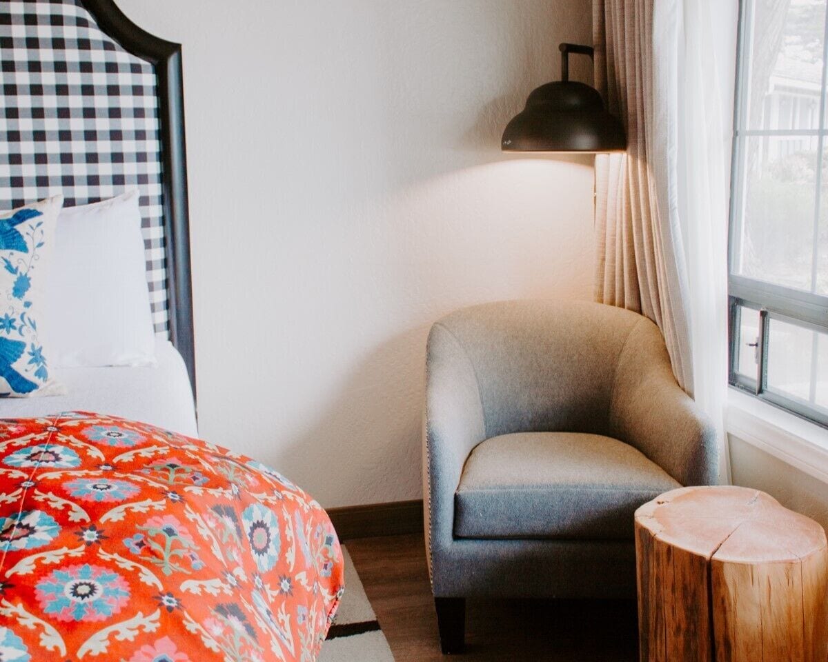 A bedroom with a bed, a chair, a bedside table, and a window.