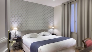 A neatly made bed with a blue blanket, two bedside lamps, a nightstand, and a chair. - Hotel Mogador Opera - Paris (Paris)