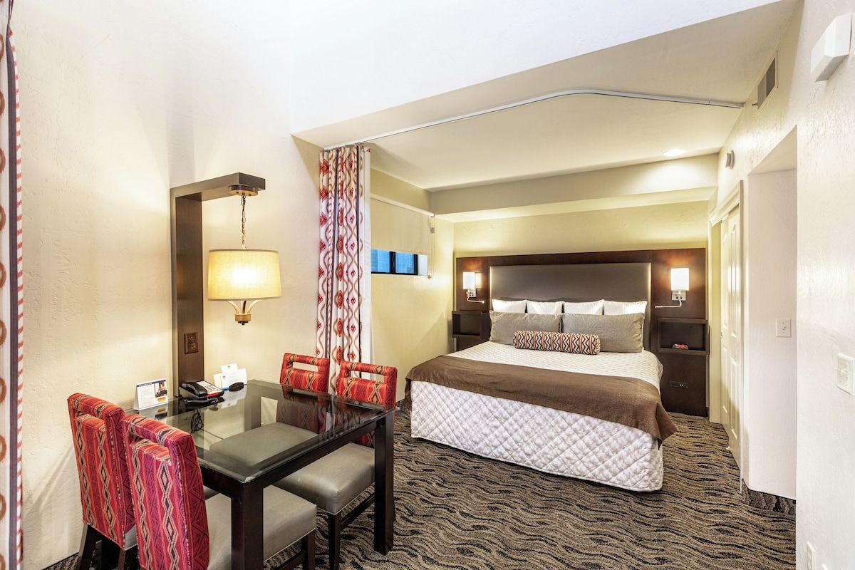 Una habitación de hotel con cama, escritorio, sillas, teléfono y lámpara.