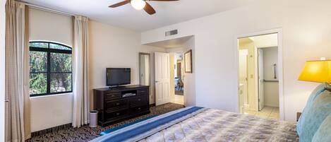 A hotel room with a bed, a ceiling fan, a television, a dresser, and a window with curtains.