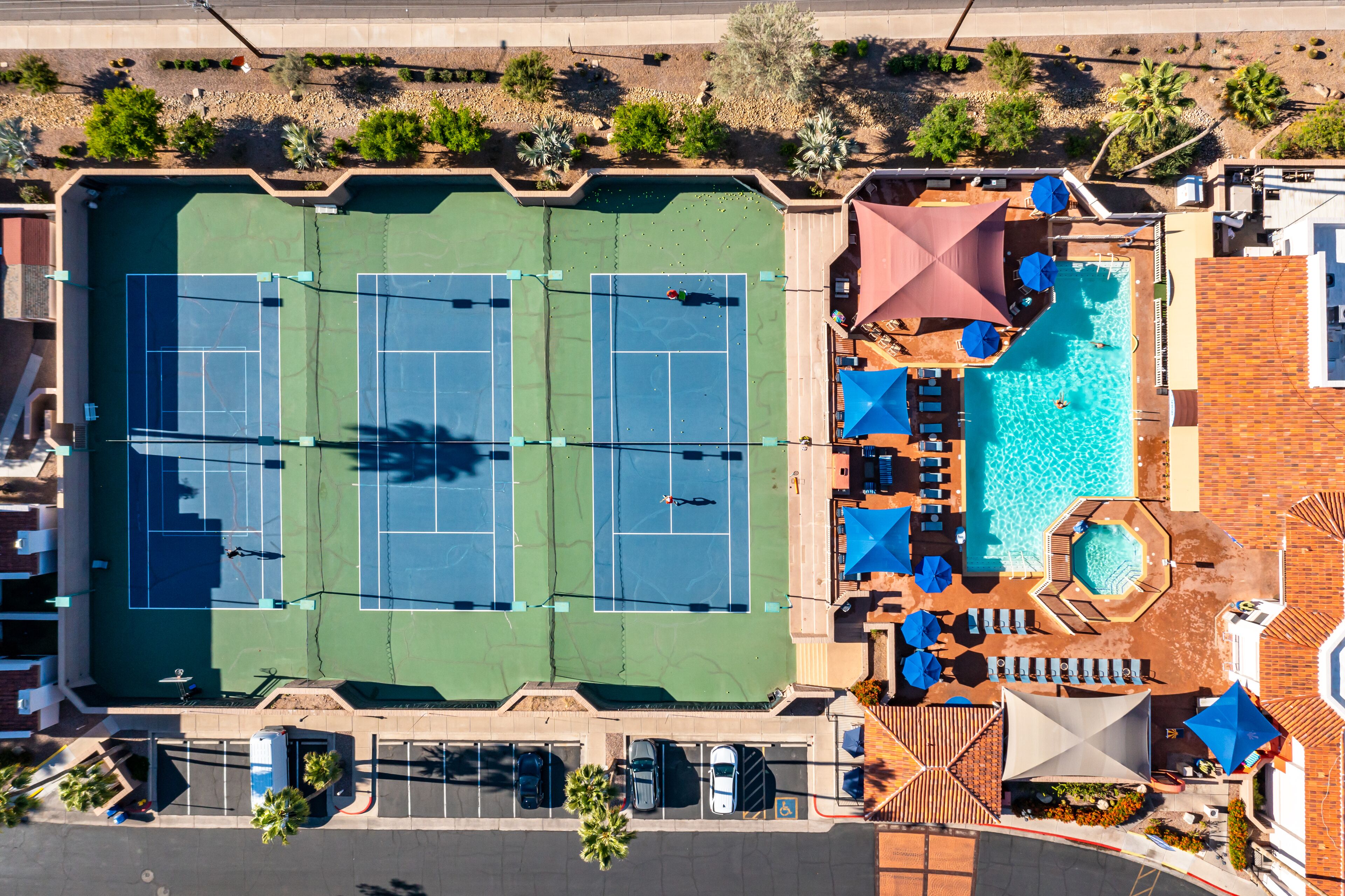 An aerial view of a hotel with two tennis courts, a swimming pool, and a parking area.
