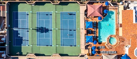 An aerial view of a hotel with two tennis courts, a swimming pool, and a parking area.