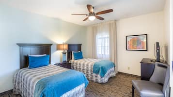 A hotel room with two beds, a ceiling fan, a desk with a chair, and a painting on the wall.
