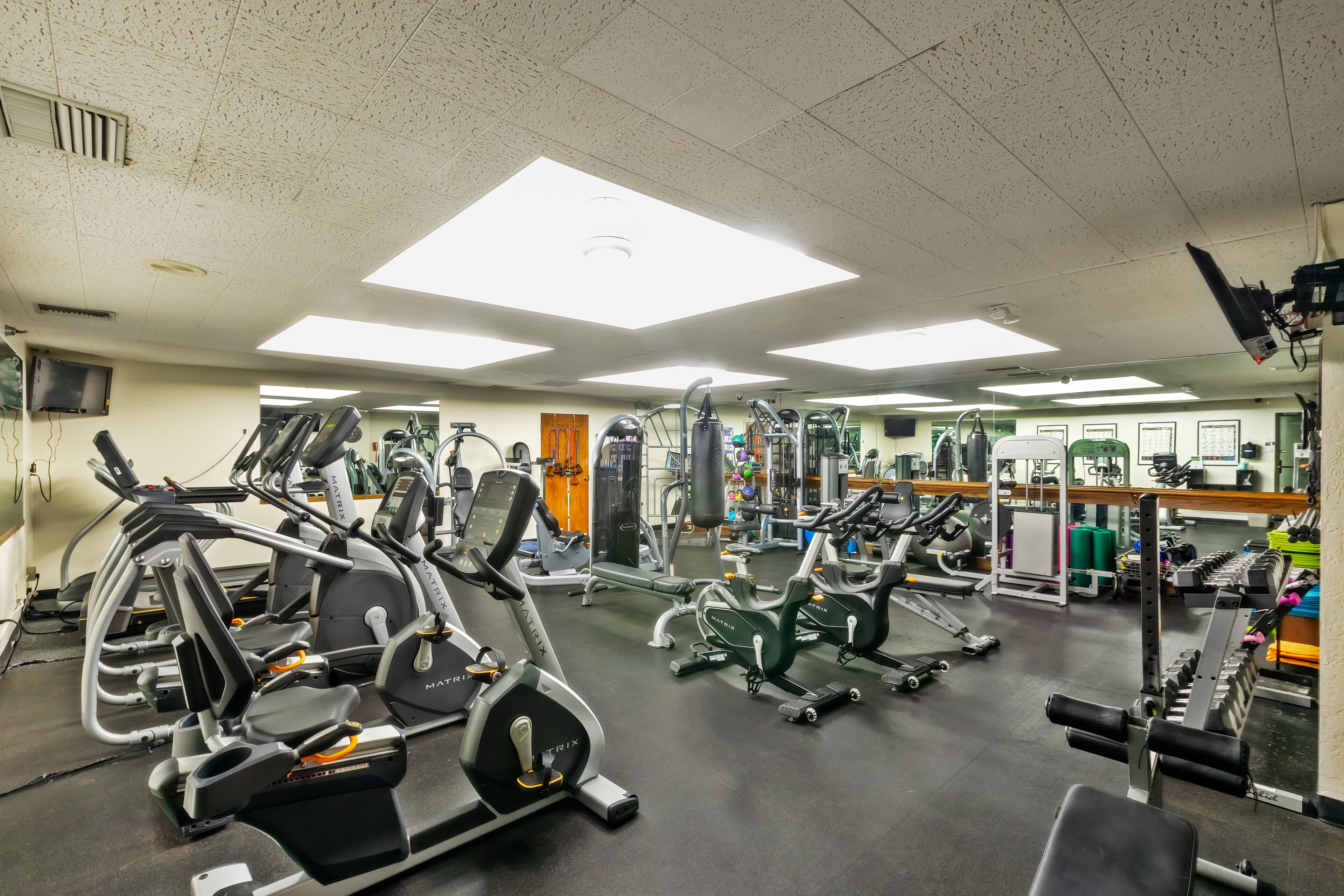 A gym with various exercise machines, mirrors, and a weightlifting area.