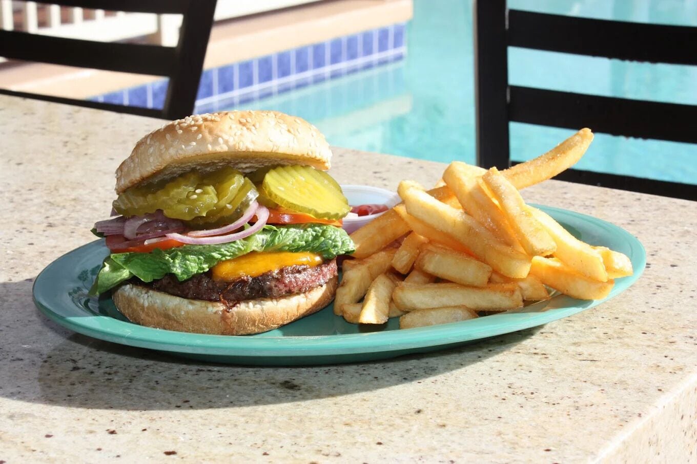 Un plato con una hamburguesa y papas fritas junto a una piscina.