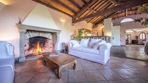 A cozy living room with a fireplace, a white sofa, and a wooden coffee table. - Hotel Monte Turri by Falkensteiner (Tortoli)
